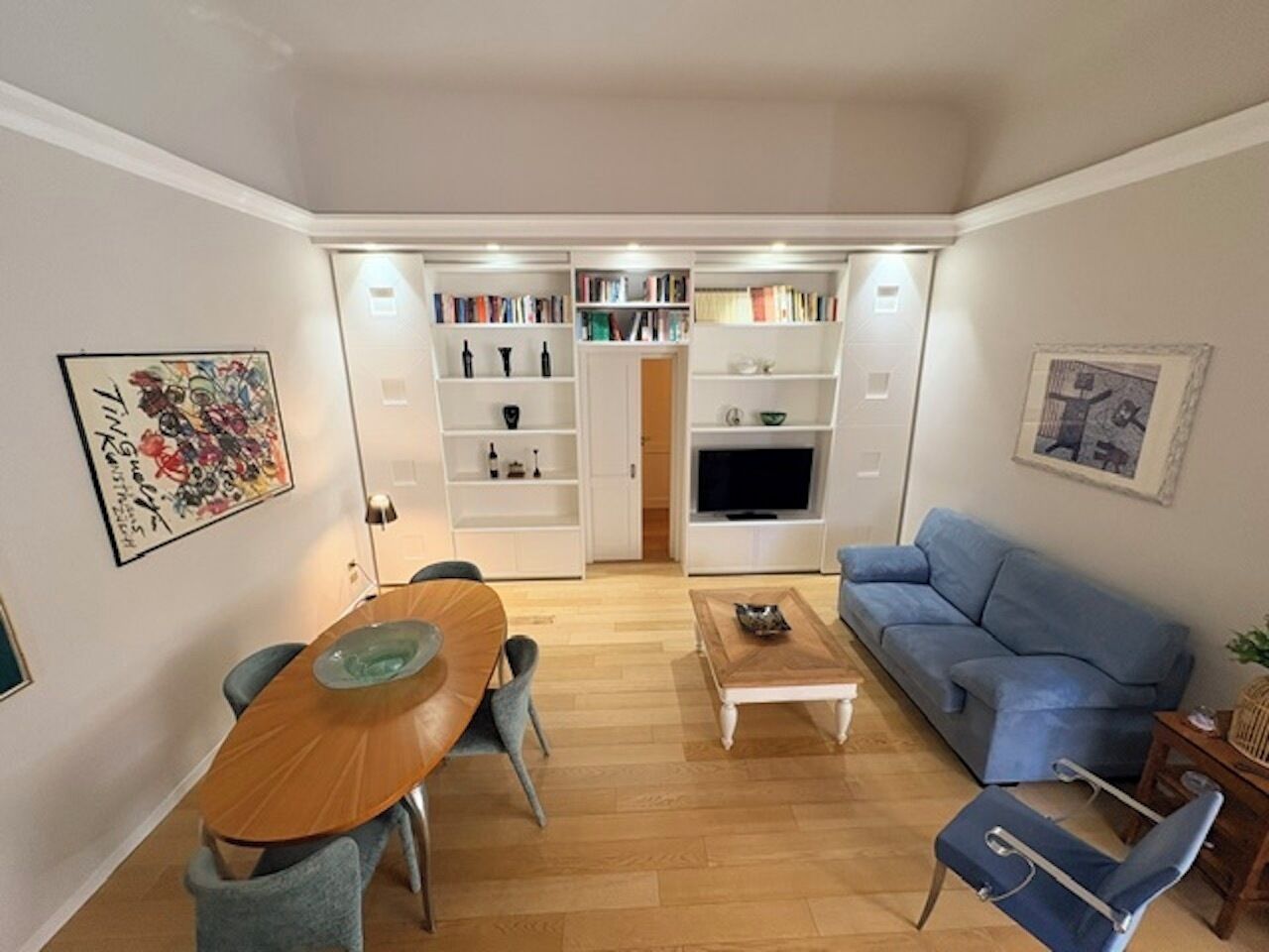 Una sala de estar con una mesa de comedor de madera, sofá azul y televisor.