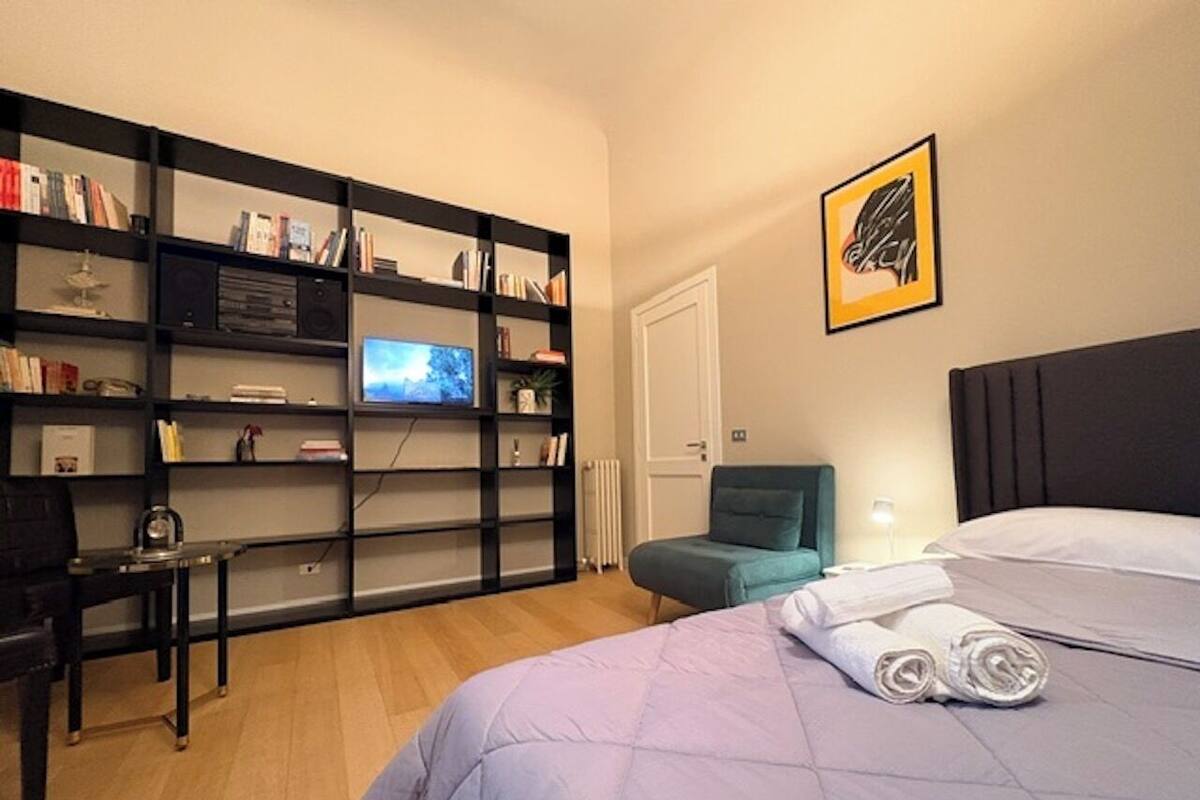 Une chambre d’hôtel comprenant un lit, un bureau, une chaise, une bibliothèque, un téléviseur et une porte.