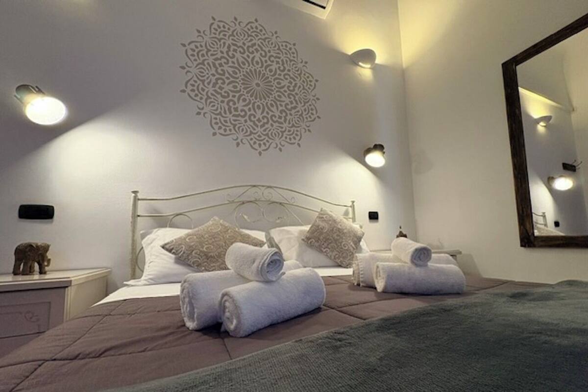 Un lit bien fait, avec des serviettes pliées, un motif décoratif sur le mur et un grand miroir.