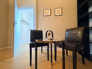 Ein Zimmer mit einem runden Tisch, zwei schwarzen Stühlen, einer kleinen Dekoration auf dem Tisch und zwei gerahmten Bildern an der Wand.