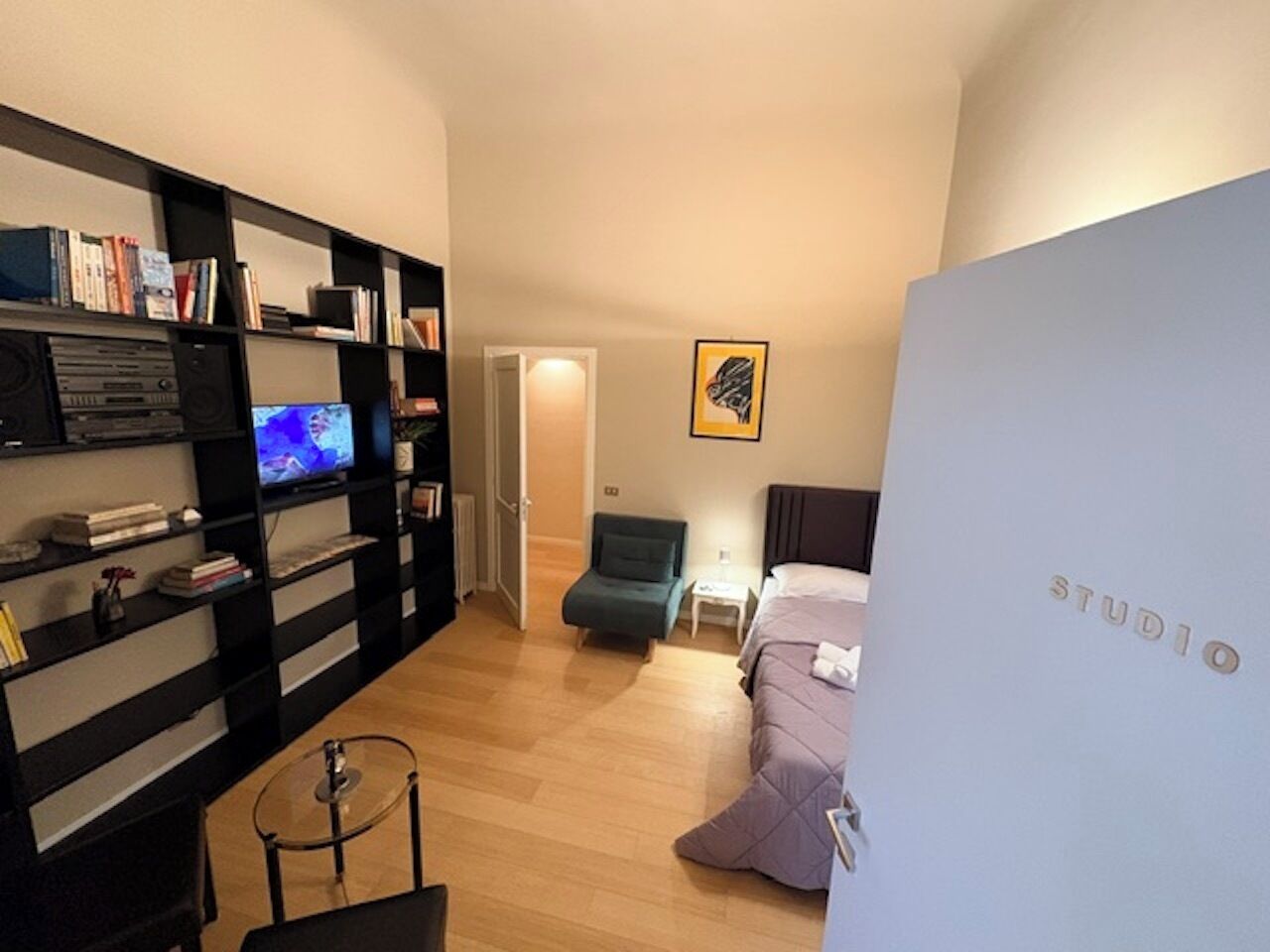 Un estudio pequeño con televisión, estantería, silla y cama.
