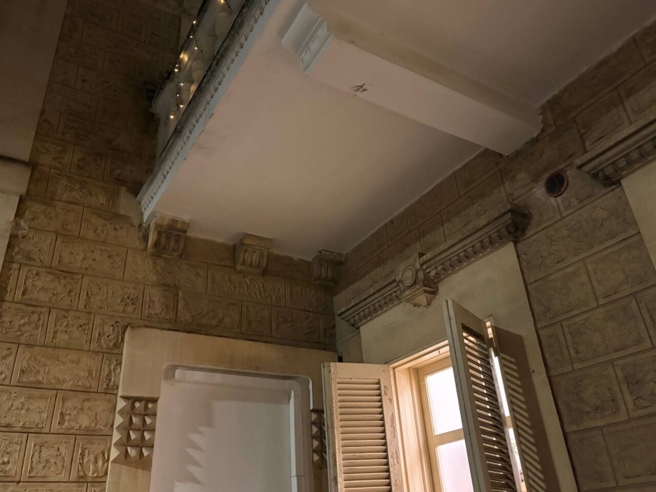 A room with stone walls, a white ceiling, and a wooden door with shutters.