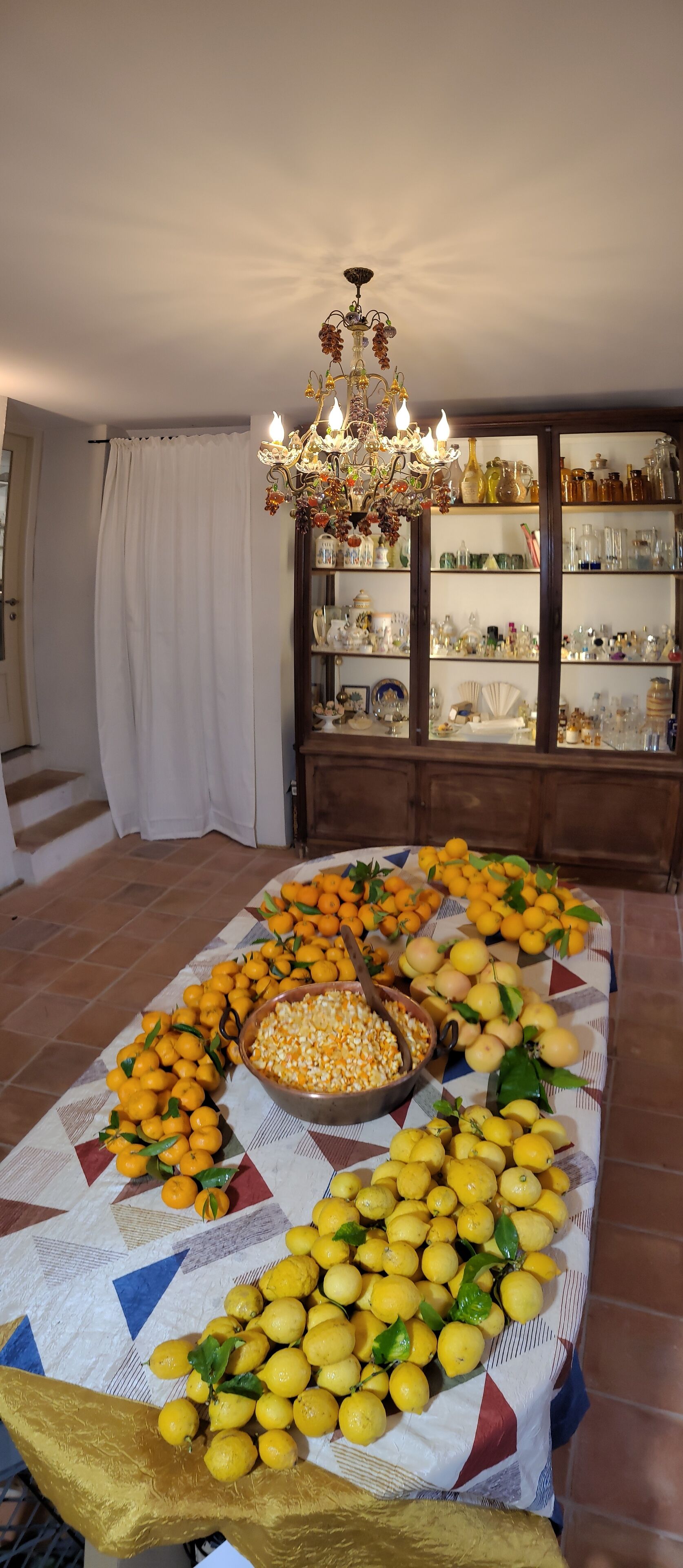 A dining table with a variety of fruits and a chandelier above.