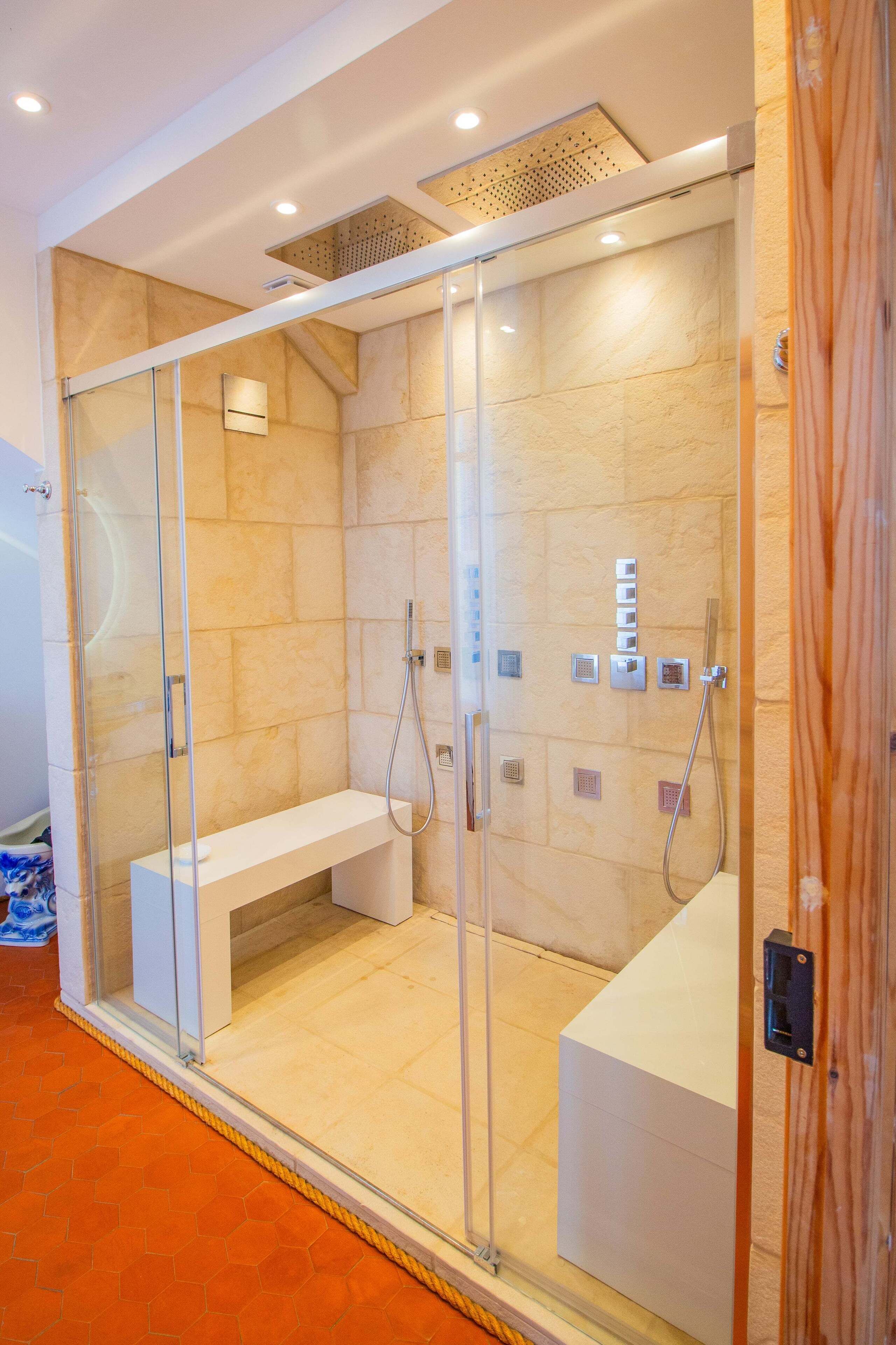 Un box de ducha moderno con puertas de vidrio, un asiento y un panel de control.