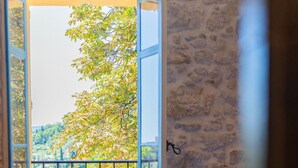 A room with a bathtub, a window with an open shutter, and a stone wall. - Domaine de la Cascade Parfumée (Grasse)