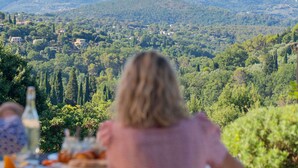 A person seated at an outdoor table with a view of a hilly landscape. - Domaine de la Cascade Parfumée (Grasse)