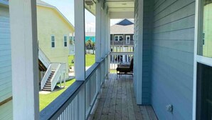A covered wooden deck with a railing, leading to a porch area with a view of neighboring houses. - The Blue Crab (Galveston)