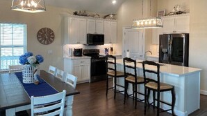 A spacious kitchen with white cabinets, a central island with bar stools, and pendant lighting. - The Blue Crab (Galveston)