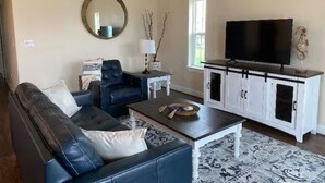 A living room with a black leather sofa, a white cabinet with a TV, and a patterned rug. - The Blue Crab (Galveston)