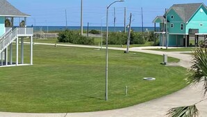 A coastal property with a grassy lawn, a pathway, and a small structure with a balcony. - The Blue Crab (Galveston)
