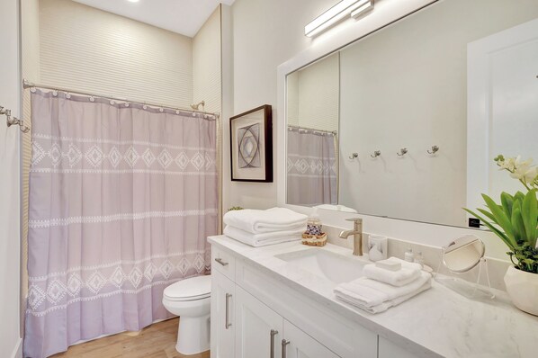 A modern bathroom with a toilet, a sink with a mirror, and a shower curtain.