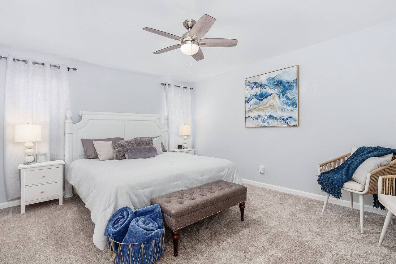 Une chambre à coucher comprenant un lit, des tables de chevet, un banc, une chaise et un ventilateur de plafond.