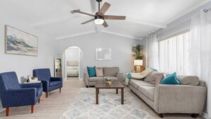 Un salon moderne doté d’un ventilateur de plafond, de deux canapés, d’une table basse et d’une grande fenêtre avec des rideaux.
