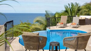 A pool area with lounge chairs and a view of the ocean.