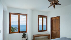 A bedroom with a large window offering a view of the sea, a wooden door, and a star-shaped ceiling light.