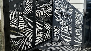 Ein modernes Gebäude mit einer Holzterrasse und einem dekorativen Metallzaun mit Blättermotiv.