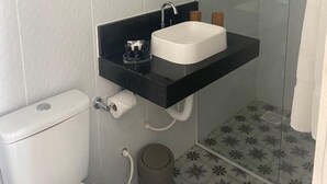 Ein Badezimmer mit Toilette, schwarzem Waschbecken mit Spiegel darüber und Duschbereich mit Glastür.