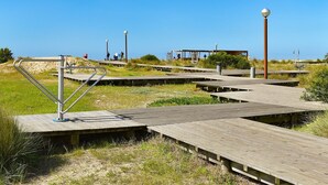 A wooden boardwalk with metal railings, leading to a covered area with benches and a lamp post.