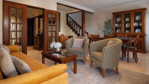 A spacious living room with a sofa, armchairs, a coffee table, and a dining area with chairs and a cabinet.