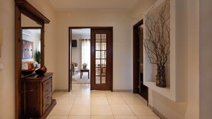A hallway with a wooden cabinet, a vase with branches, and a door leading to another room.