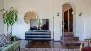 Ein Wohnzimmer mit einer Couch, einem Fernseher, einer großen Pflanze und einer Treppe, die in einen anderen Raum führt.