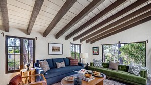 Ein geräumiges Wohnzimmer mit hoher Decke und freiliegenden Balken, ausgestattet mit einem blauen Sofa, einem grünen Sofa und einem Holztisch.