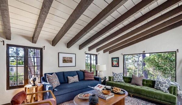 A spacious living room with a high ceiling and exposed beams, furnished with a blue sofa, a green sofa, and a wooden coffee table.
