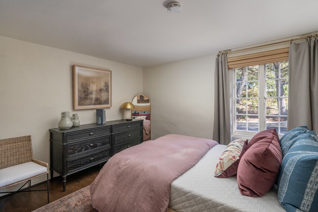 A bedroom with a bed, a dresser, a chair, a window with curtains, and a framed picture on the wall.