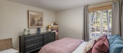 A bedroom with a bed, a dresser, a chair, a window with curtains, and a framed picture on the wall.