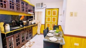 Een compacte keuken met donkerhouten kastjes, een eettafel voor vier personen en een geel accentmuur.