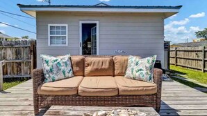 A small house with a porch, a wicker sofa with cushions, and a wooden deck. - The Beach Box is located in the heart of CB, walking distance to the boardwalk! (Carolina Beach)