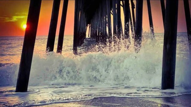 A pier extending into the ocean with waves crashing against it. - The Beach Box is located in the heart of CB, walking distance to the boardwalk! (Carolina Beach)