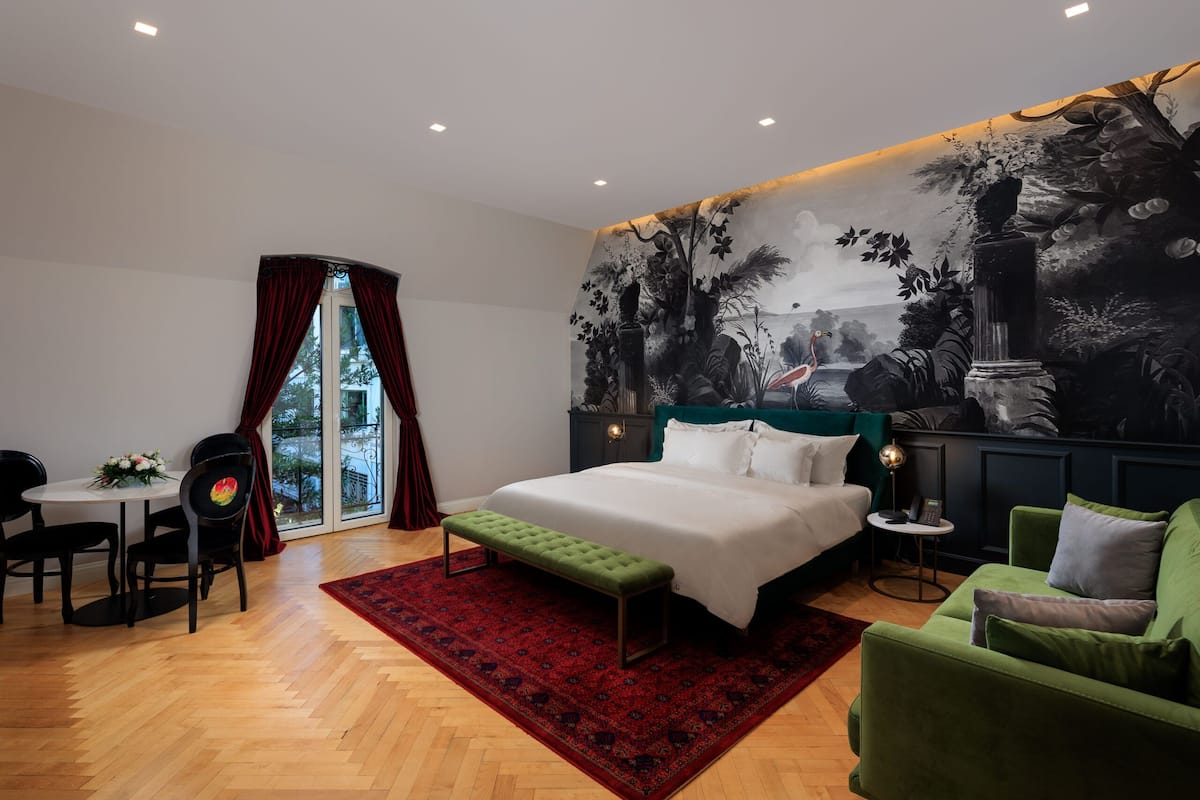 Un dormitorio con cama, sillón verde, mesa de comedor con sillas y una alfombra roja.