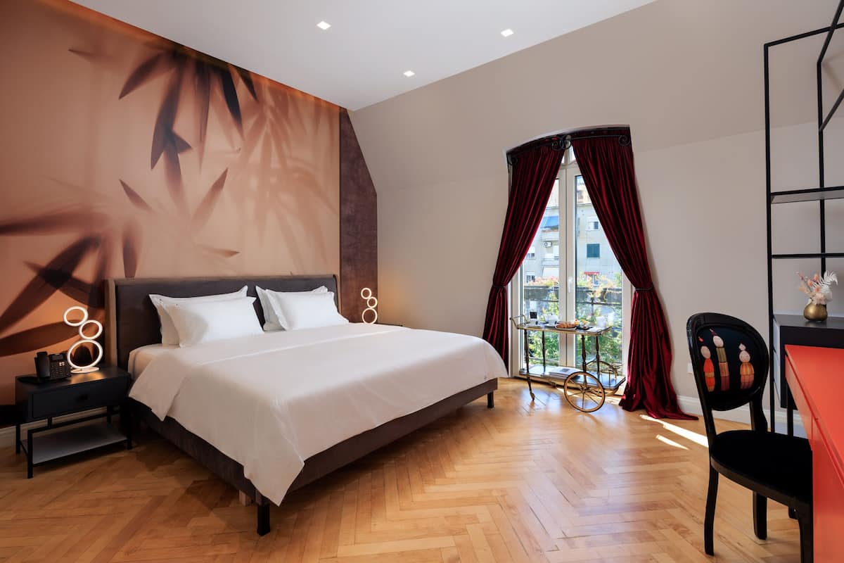Una habitación de hotel moderna con una cama grande, una mesita de noche, un escritorio y un ventanal con vistas a la ciudad.