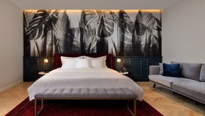 A bedroom with a large bed, a red patterned rug, a grey sofa, and a wall with a large black and white leaf mural. - Arté Boutique Hotel (Tirana)