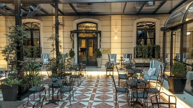 An outdoor cafe area with tables and chairs, potted plants, and a patterned floor. - Arté Boutique Hotel (Tirana)