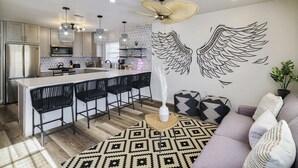 A modern kitchen with a central island, bar stools, a ceiling fan, and a decorative wall mural. - Imani Playce: Perfect location w/ Boho Vibes! (Atlantic City)