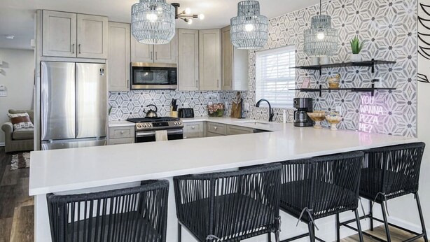 A modern kitchen with a large island, stainless steel appliances, and black wicker bar stools. - Imani Playce: Perfect location w/ Boho Vibes! (Atlantic City)