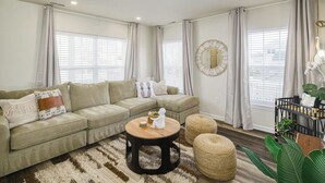 A modern living room with a sectional sofa, a round coffee table, and a large mirror on the wall. - Imani Playce: Perfect location w/ Boho Vibes! (Atlantic City)