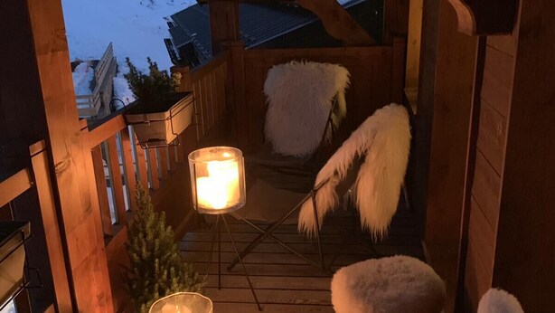 A wooden deck with a cozy seating area, two lit candles, and a small Christmas tree.