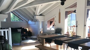 A spacious loft-style room with a high ceiling, wooden beams, a large dining table, and a cozy seating area.