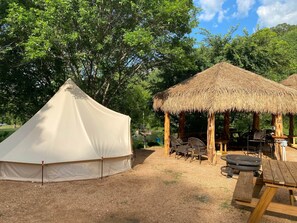 Relax in a spacious tent surrounded by lush greenery, with a nearby pavilion offering a dining or socializing space.