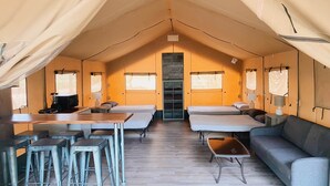 A tented accommodation with two beds, a sofa, a table with chairs, and a kitchenette.