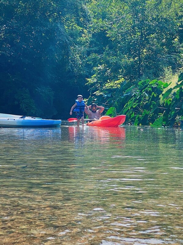 A calm river with two kayaks, one blue and one red, and a person in a blue life jacket.