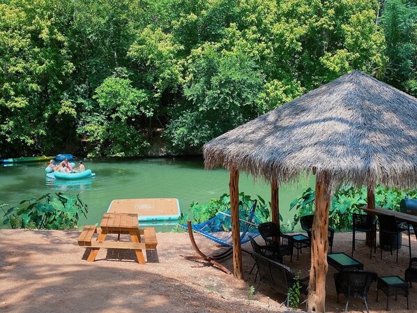 Relax by the river at this serene riverside retreat, where a shaded pavilion offers a peaceful spot for dining and relaxation.