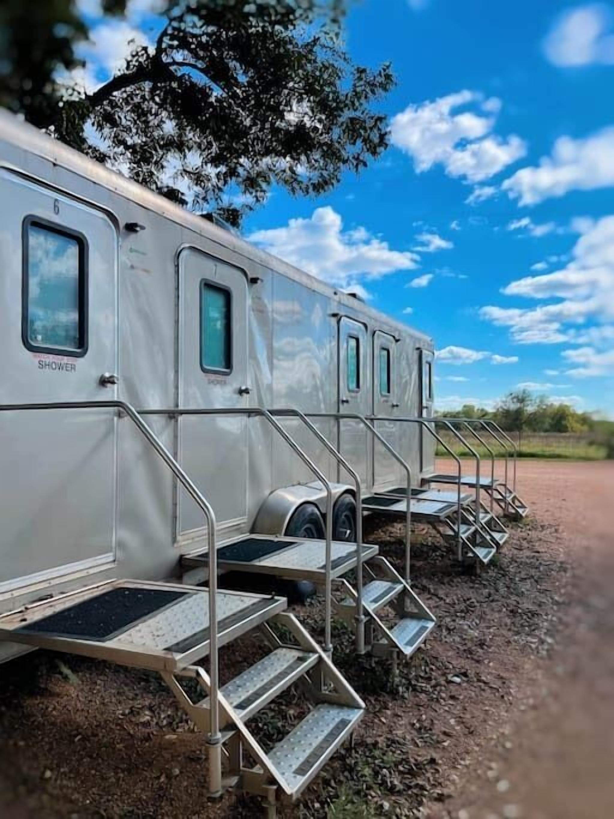 A row of motorhomes parked on a dirt path with metal steps leading up to the doors.
