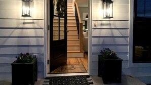 Une porte d’entrée avec un escalier en bois menant à l’intérieur, de part et d’autre duquel se trouvent deux lanternes noires et deux jardinières.