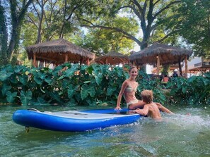 Un área de piscina con una balsa inflable azul, rodeada de vegetación tropical y estructuras con techo de paja.