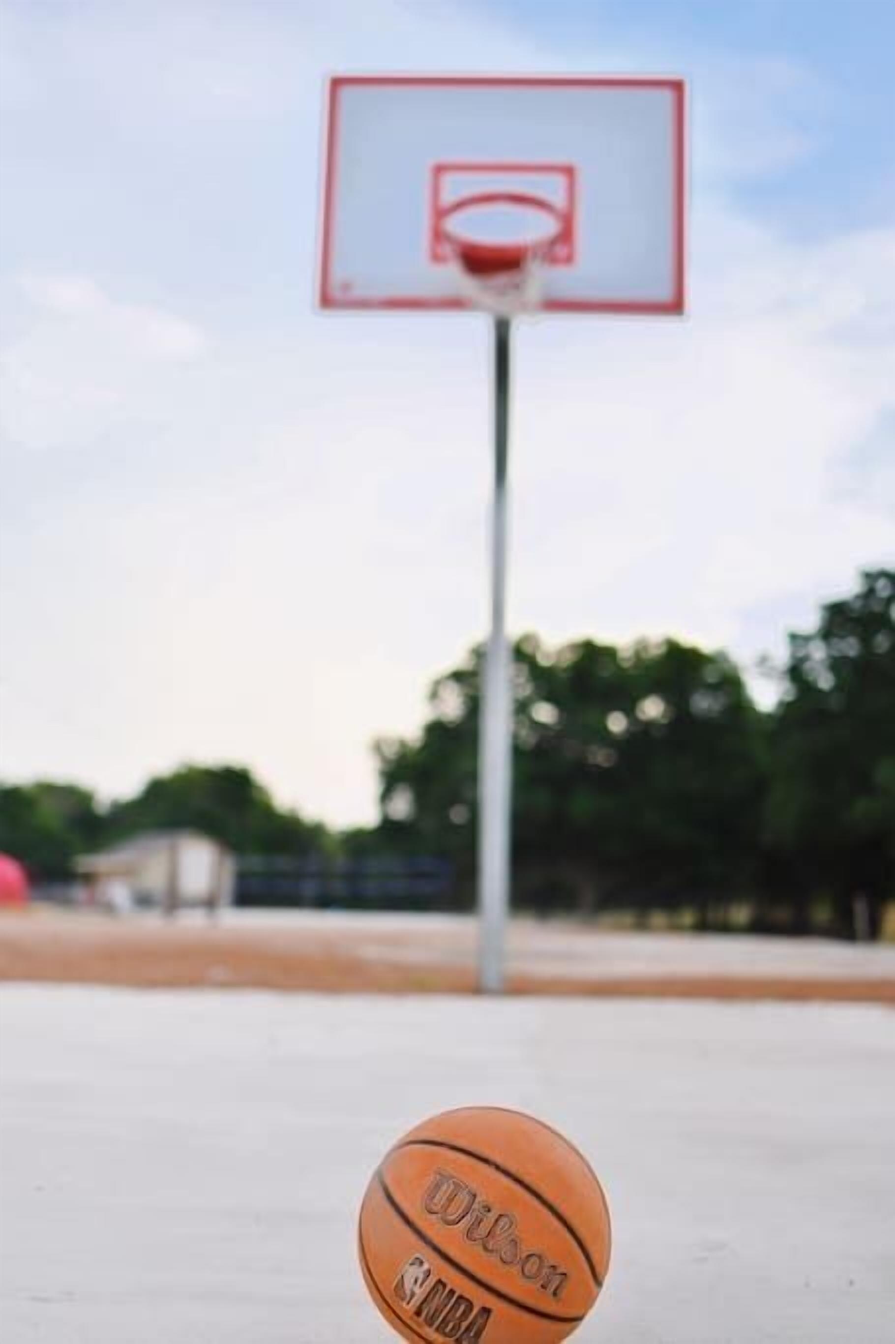 Un panier de basket avec un filet, un ballon de basket et un ciel dégagé en arrière-plan.