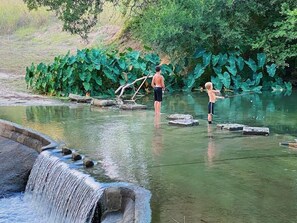 A natural water feature with a small waterfall, surrounded by lush greenery and rocks. - #23Son’s Rio Cibolo Deluxe Safari Cabin (Marion)